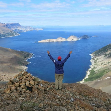 TA standing with arms raised overlooking the Labrador Sea from a high viewpoint