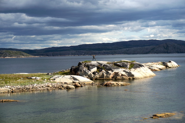 A person jumping into the air on a rocky outcrop surrounded by water