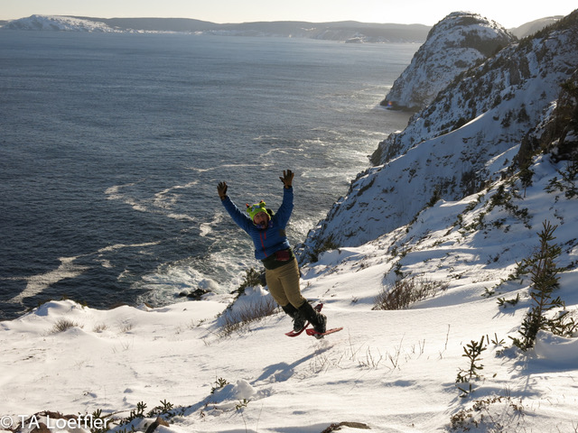 TA is midair with arms outstretched jumping on snowshoes.